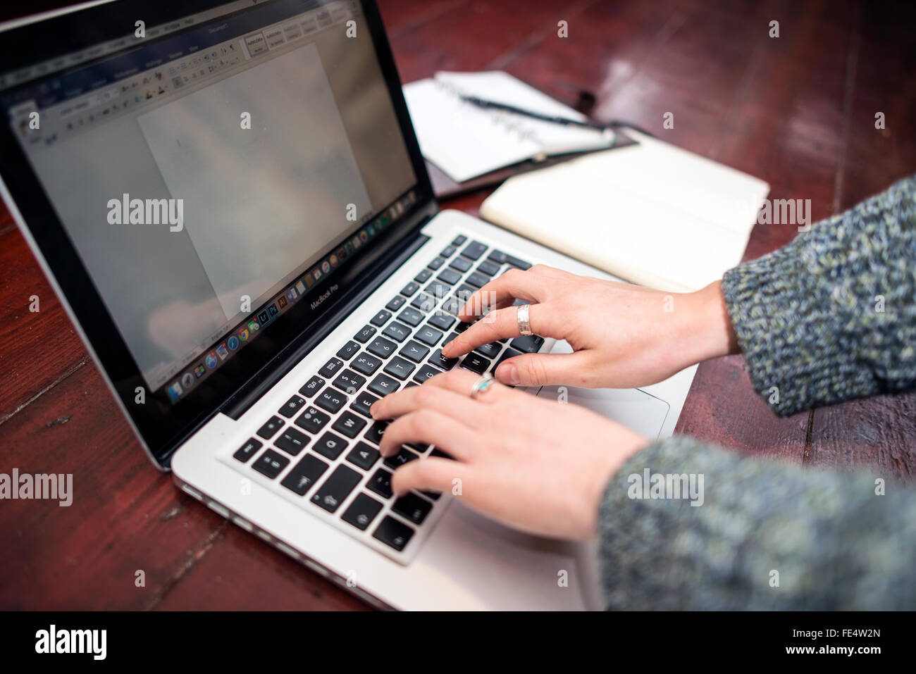 Person Tying on a Macbook with Notepad and Diary Stock Photo