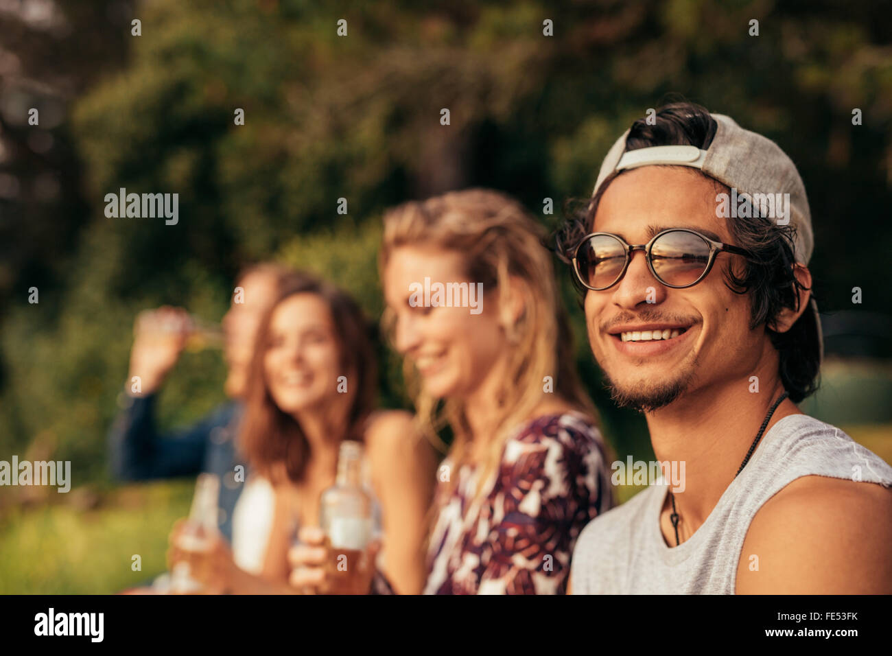 Portrait of happy young man at a lake with friends sitting by. Young friends hanging out at the lake. Stock Photo