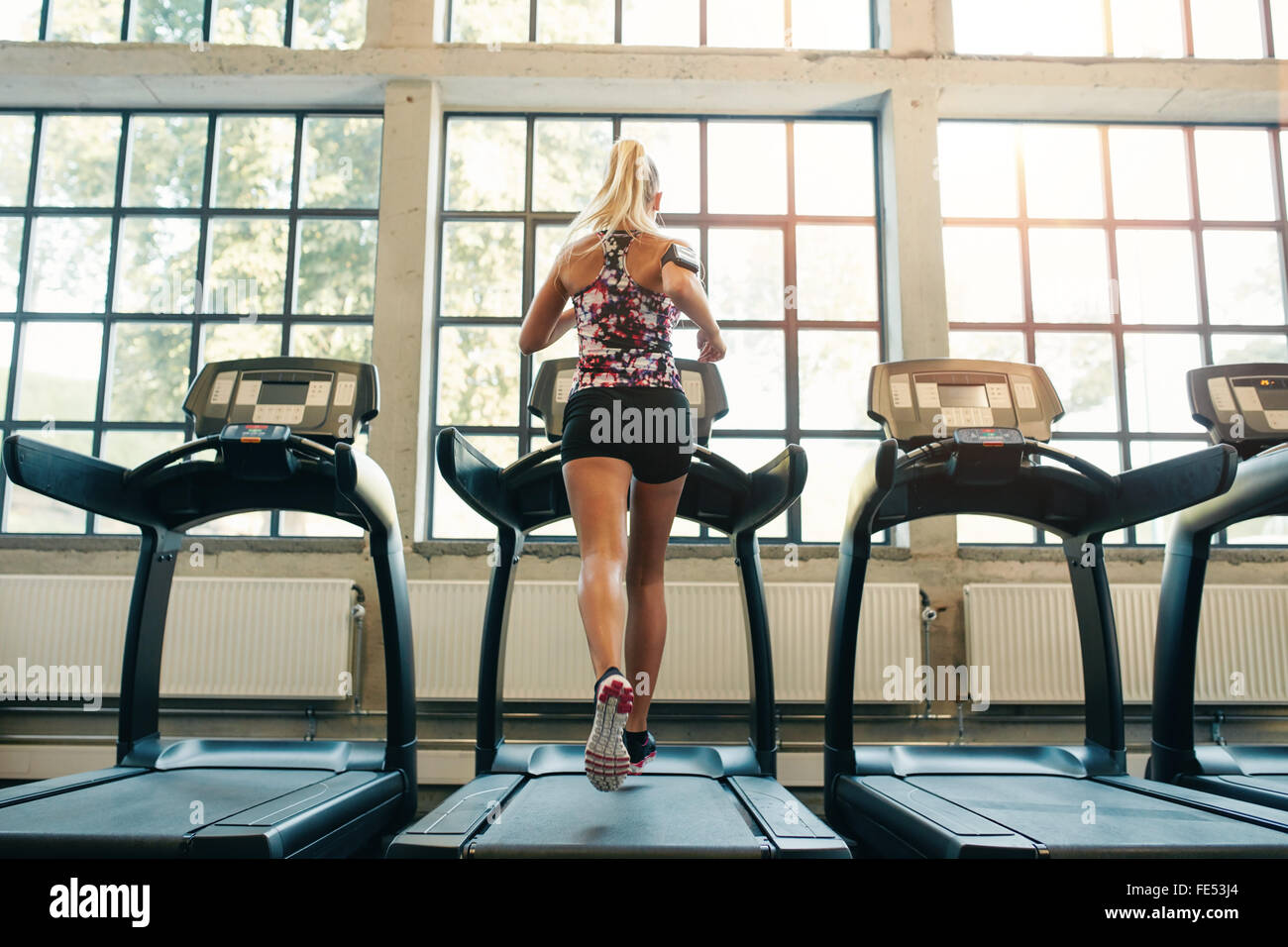 Horizontal shot of woman jogging on treadmill at health club. Female working out at a gym running on a treadmill. Stock Photo