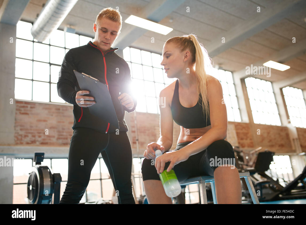 Personal coach standing near young woman and showing something on his clipboard. Caucasian female relaxing and talking with pers Stock Photo