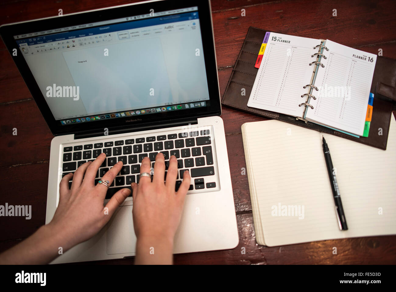 Person Tying on a Macbook with Notepad and Diary Stock Photo