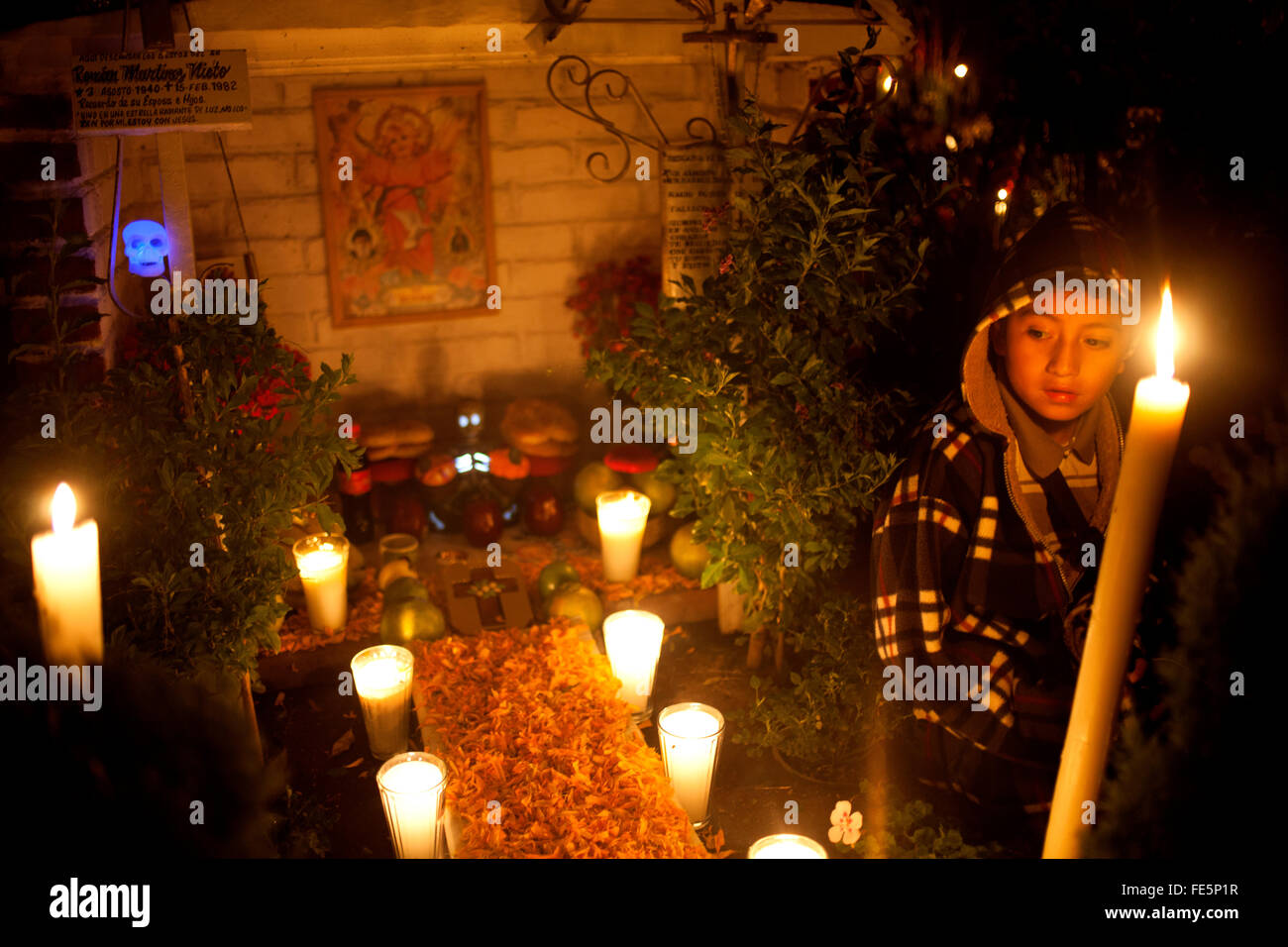A boy sits in a tomb decorated with candles and yellow marigold flowers