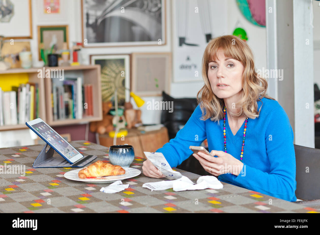 Woman checks the receipts and looks confused at a living room table. Stock Photo