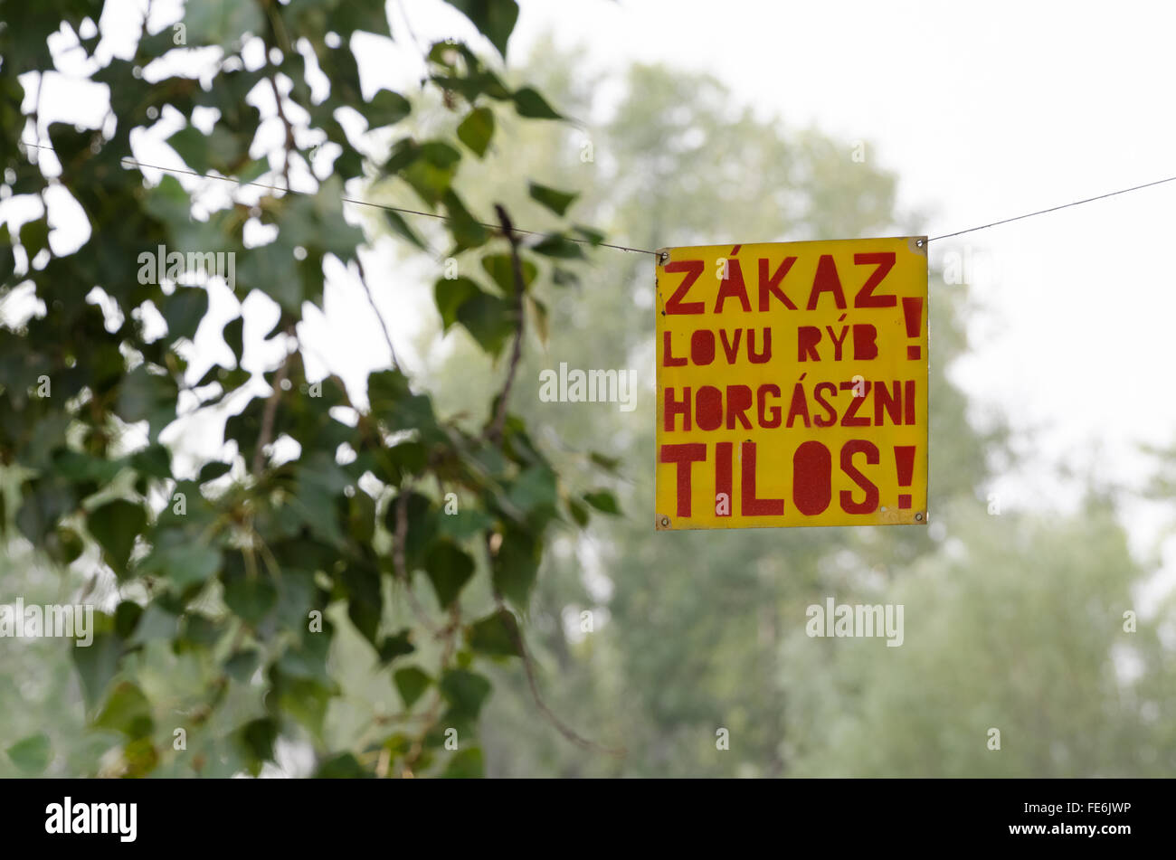 Red on Yellow Hanging Sign on Tree about Fishing Prohibition Bilingual Slovak and Hungarian Stock Photo