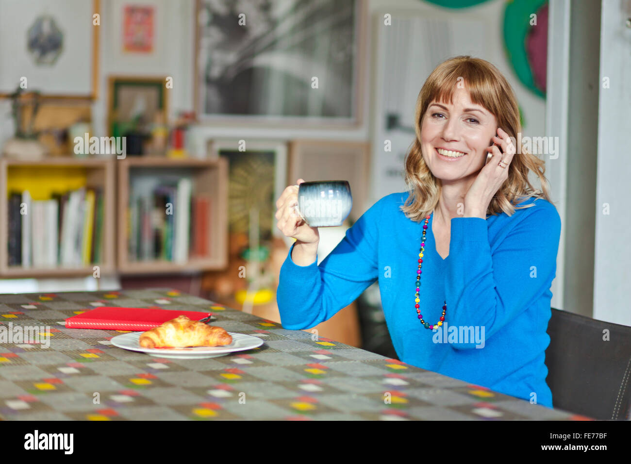 Woman talks on the phone at the living room table. Stock Photo