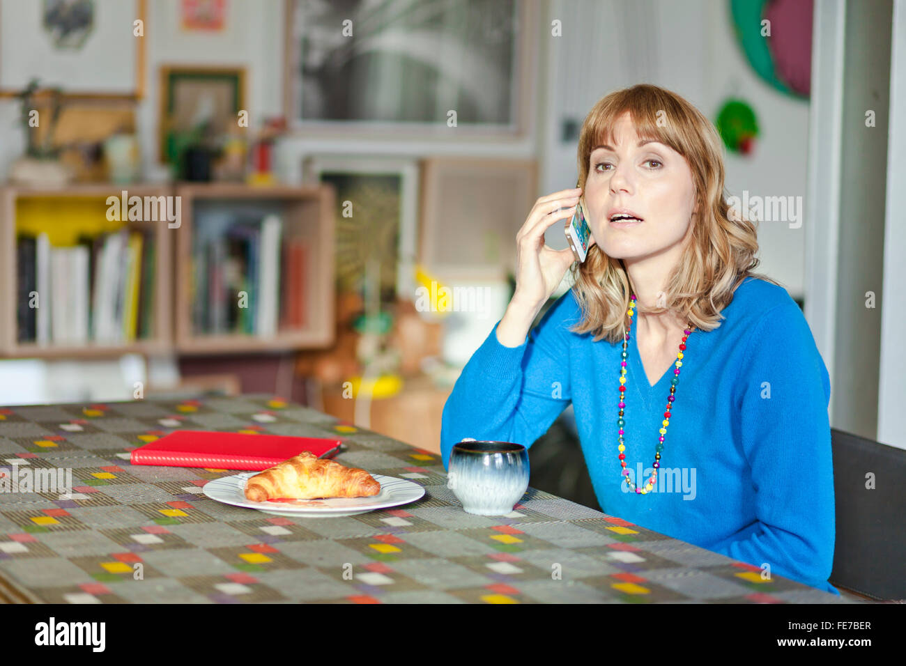 Woman talks on the phone at the living room table. Stock Photo