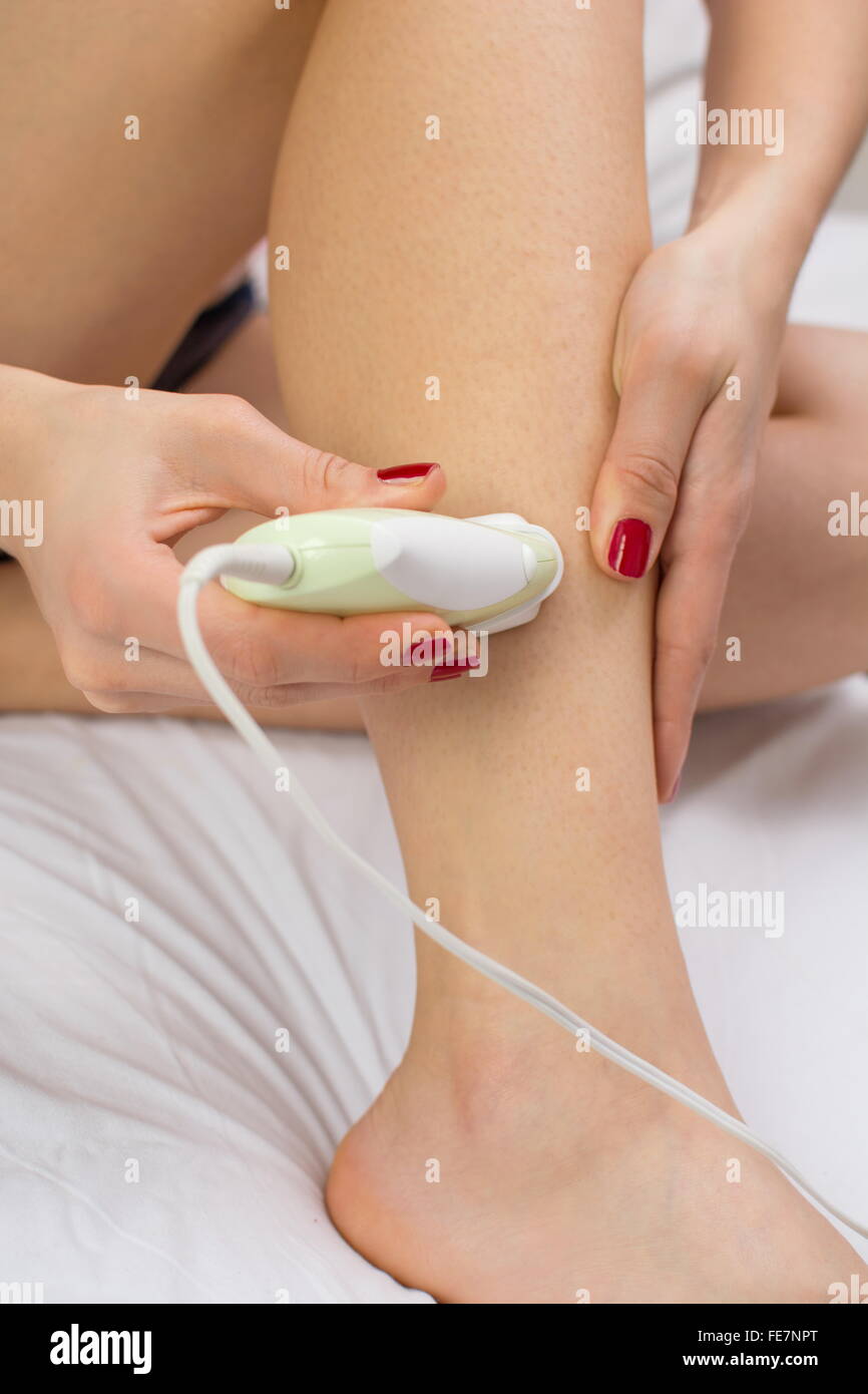Girl epilates her leg with an epilator on the bed Stock Photo