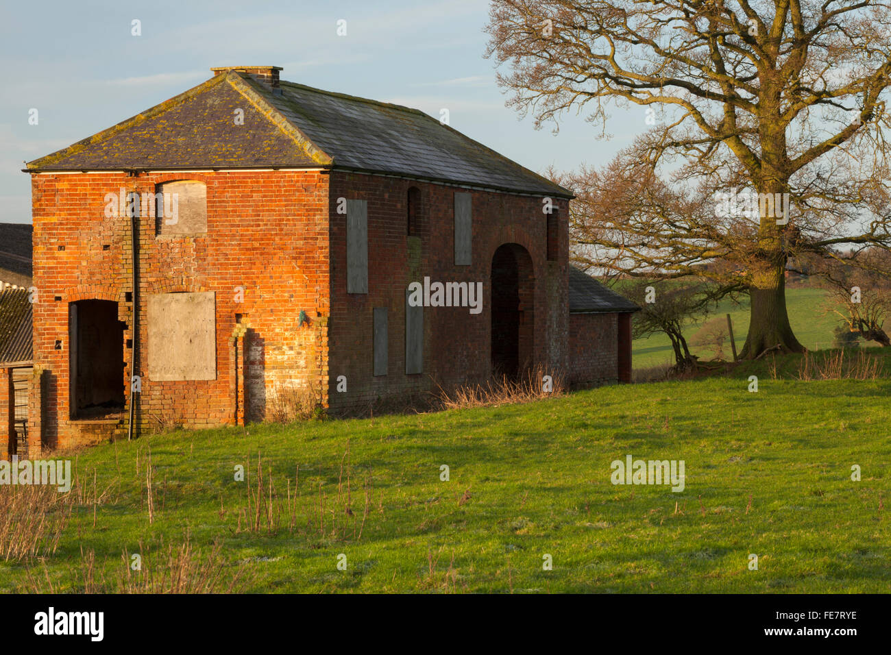 An old deserted farmhouse with boarded up windows and brickwork bathed in winter sunshine, Northamptonshire, England Stock Photo