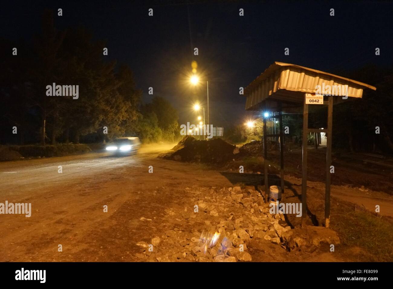 Illuminated Car On Dirt Road Passing By Bus Stop At Night Stock Photo