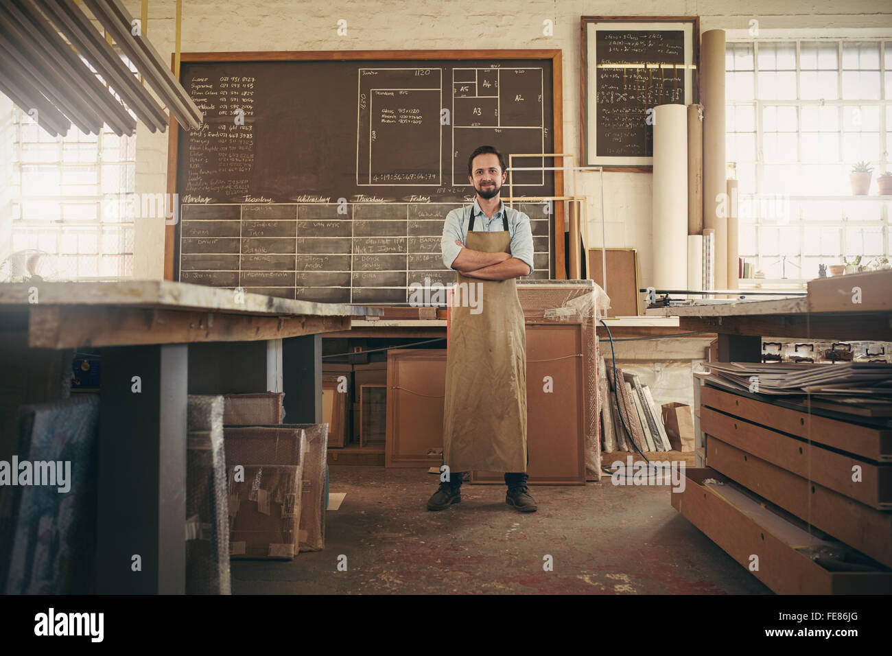 Full length portrait of a desigern craftsman confidently standing with his arms crossed in his workshop and smiling at the camer Stock Photo