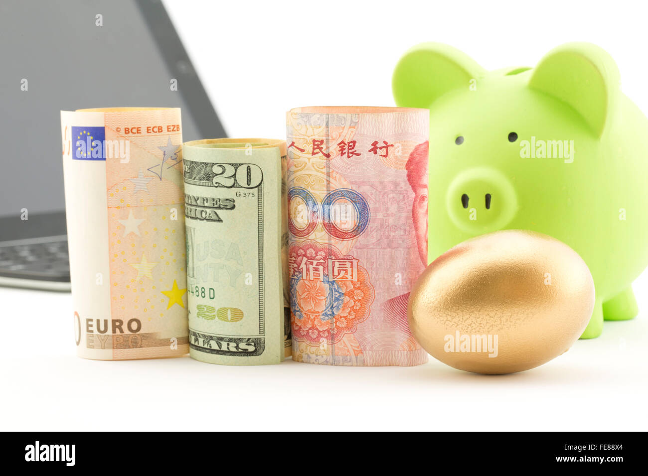 Three currencies, euro, dollar, and yen, placed with gold nest egg with computer and bank in background. Stock Photo