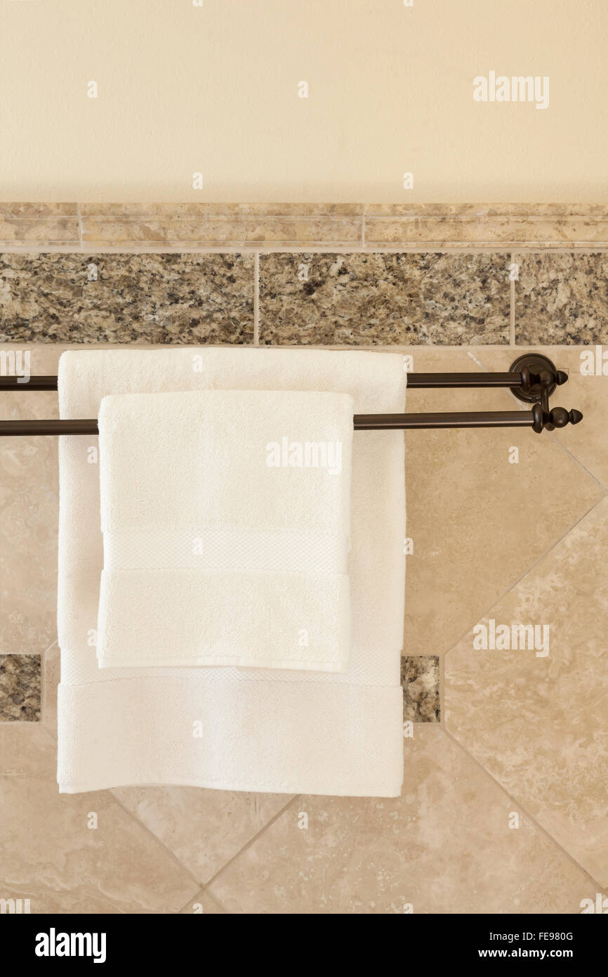 Clean white cotton towels on bronze towel bars in luxury bathroom with stone tile walls. Upscale