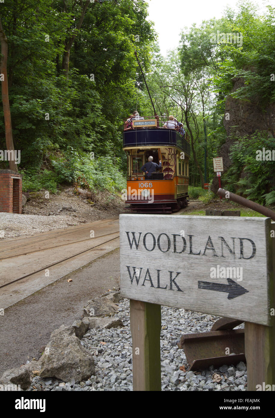 Glasgow Tram departs at Crich Tramway Museum with a sign in the foreground directing visitors to the Woodland Walk sculptures Stock Photo