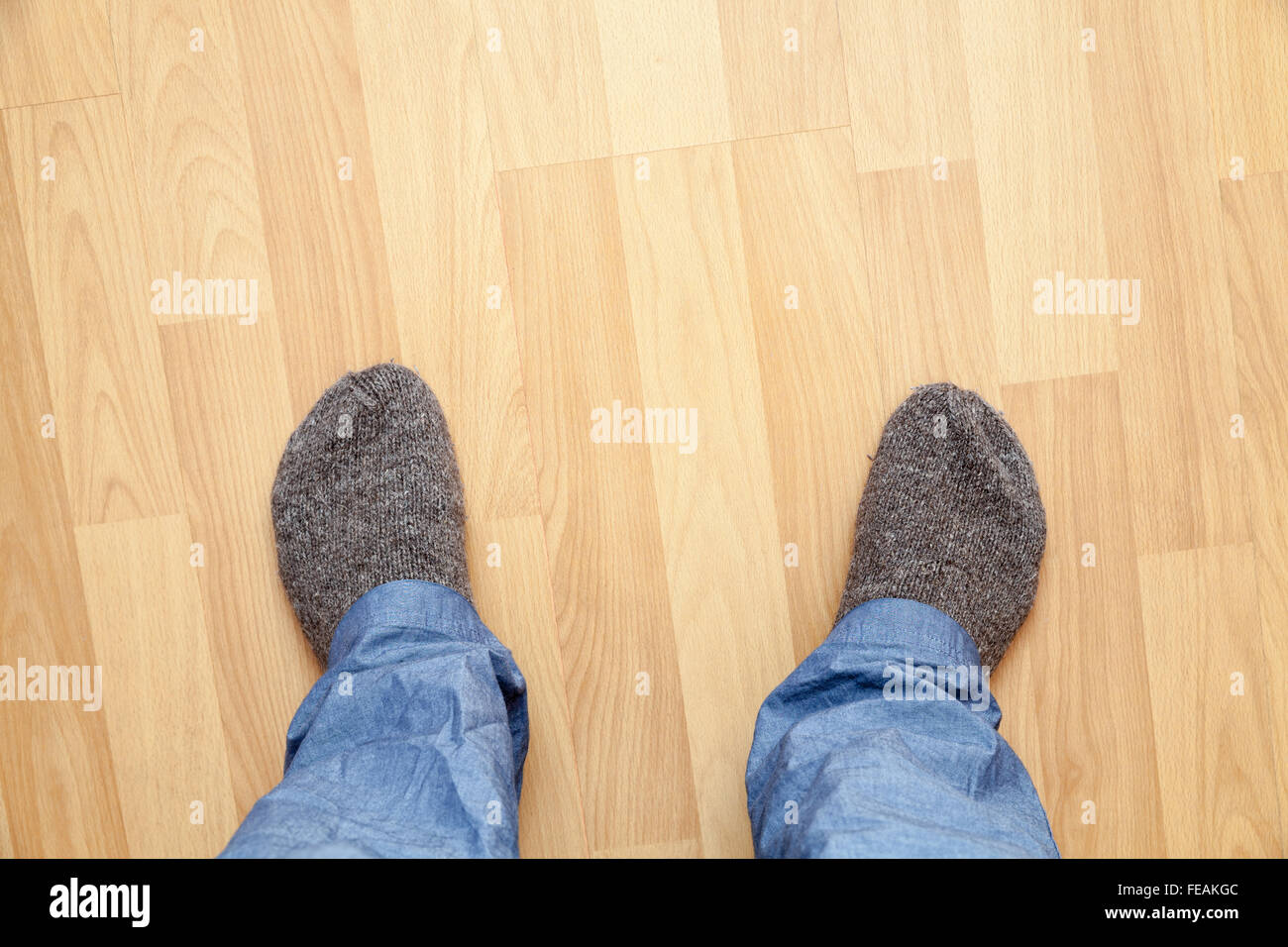 Male feet in blue pants and gray woolen socks stand on wooden parquet Stock Photo