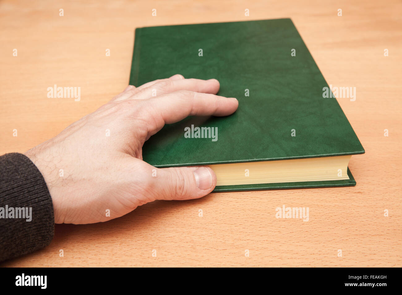 Male hand and book with empty dark green leather cover lay on wooden desk Stock Photo