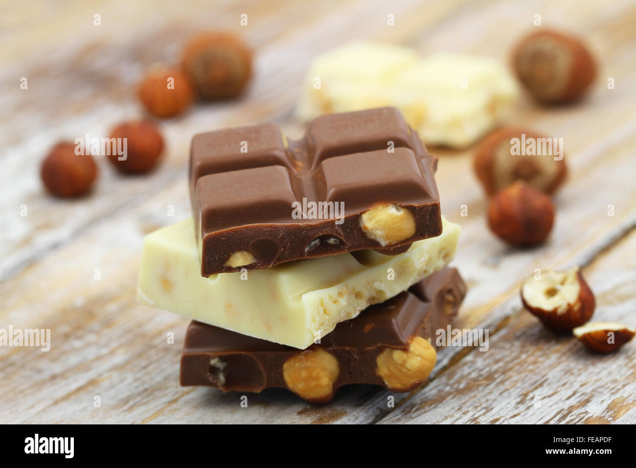 Milk and white chocolate pieces with whole hazelnuts stacked up on wooden surface Stock Photo