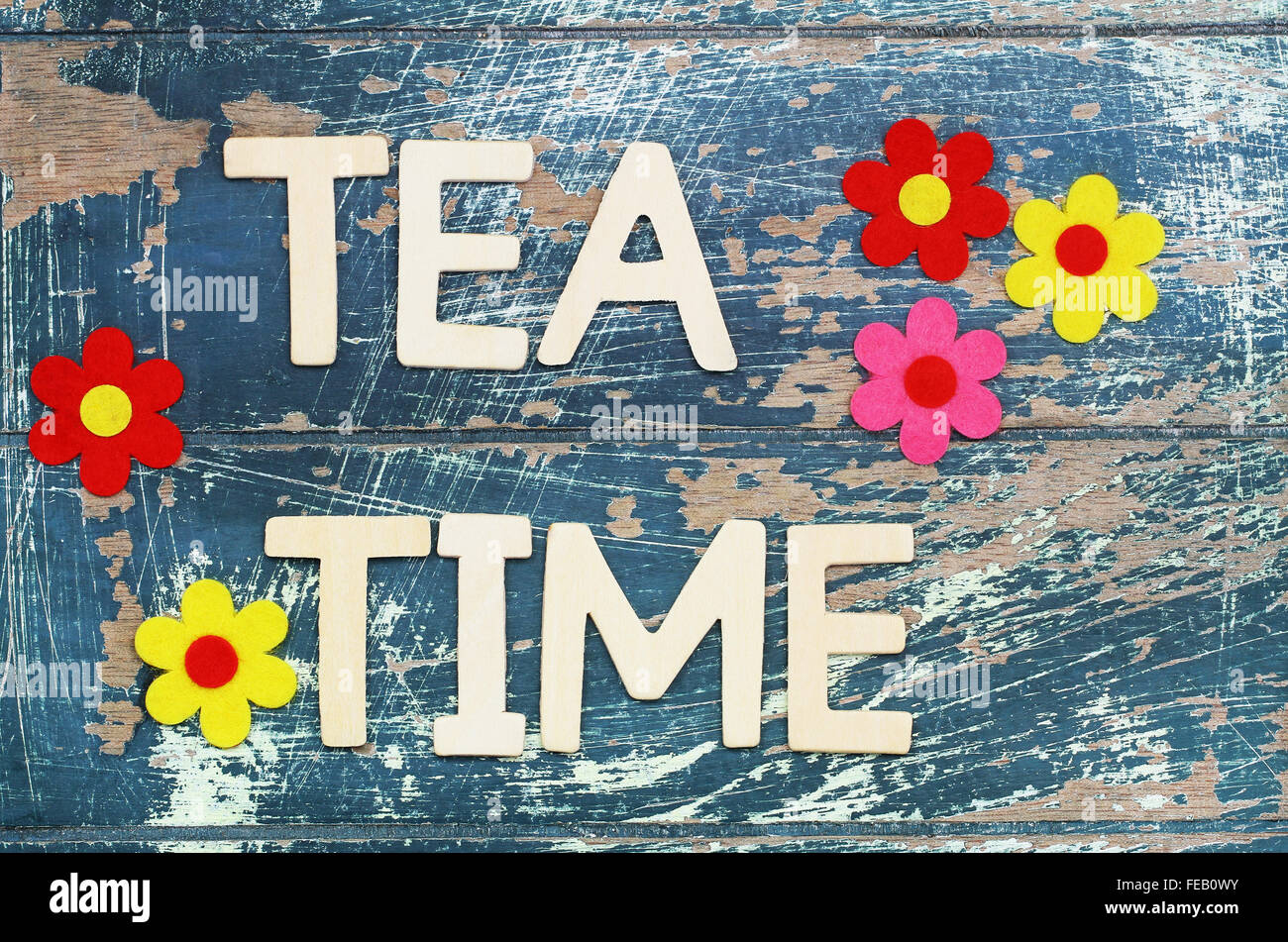 Tea time written with wooden letters on rustic surface and colorful flowers Stock Photo