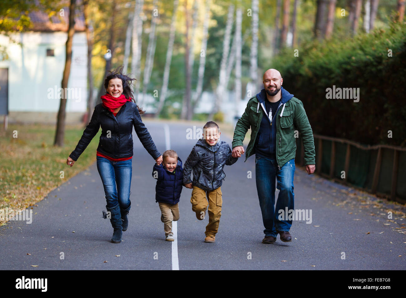 Happy family running on the road in a park at autumn time Stock Photo