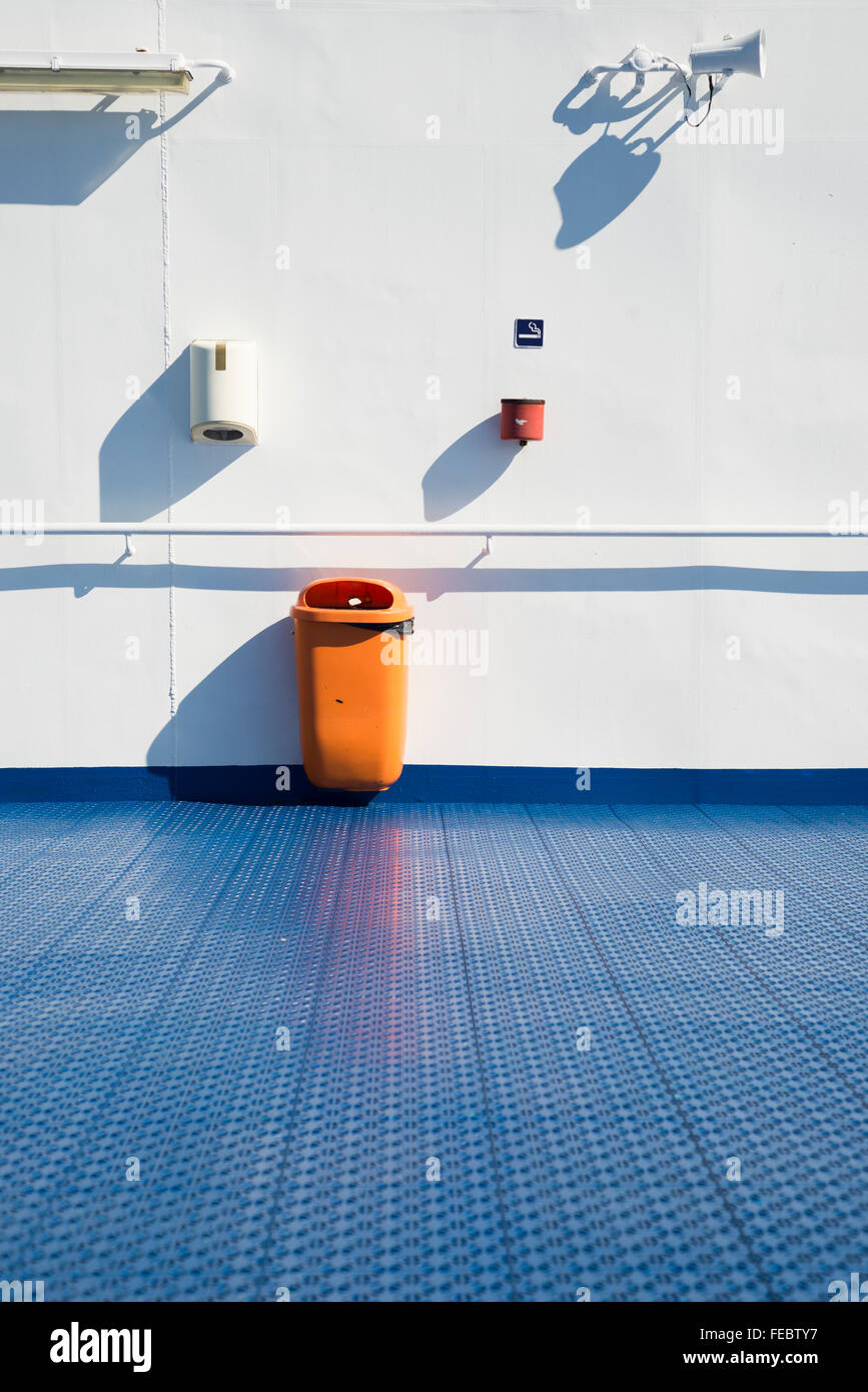 Loudspeaker,rubbish bin,ashtray,lamp and paper distributor on white wall behind blue floor on the outer deck of a passenger ship Stock Photo