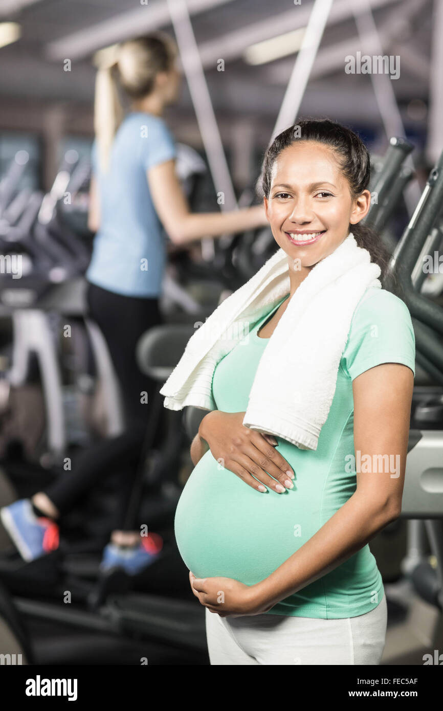 Smiling pregnant woman with towel around neck touching belly Stock