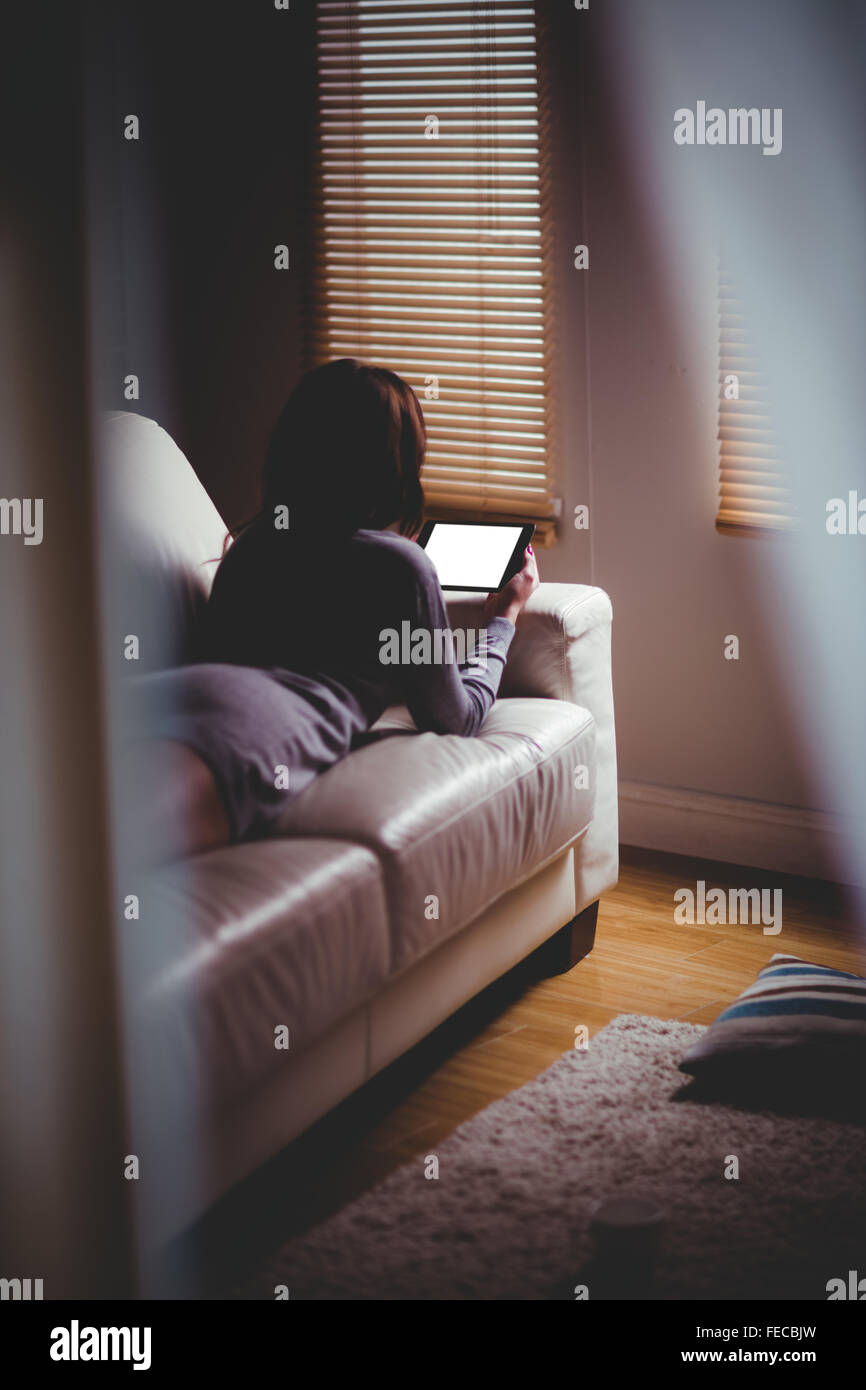 Beautiful brunette using tablet lying on the couch Stock Photo - Alamy