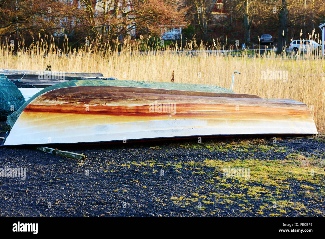 One plastic boat turned upside down on land during winter. The keel is very discolored after years of use. Reeds in background. Stock Photo