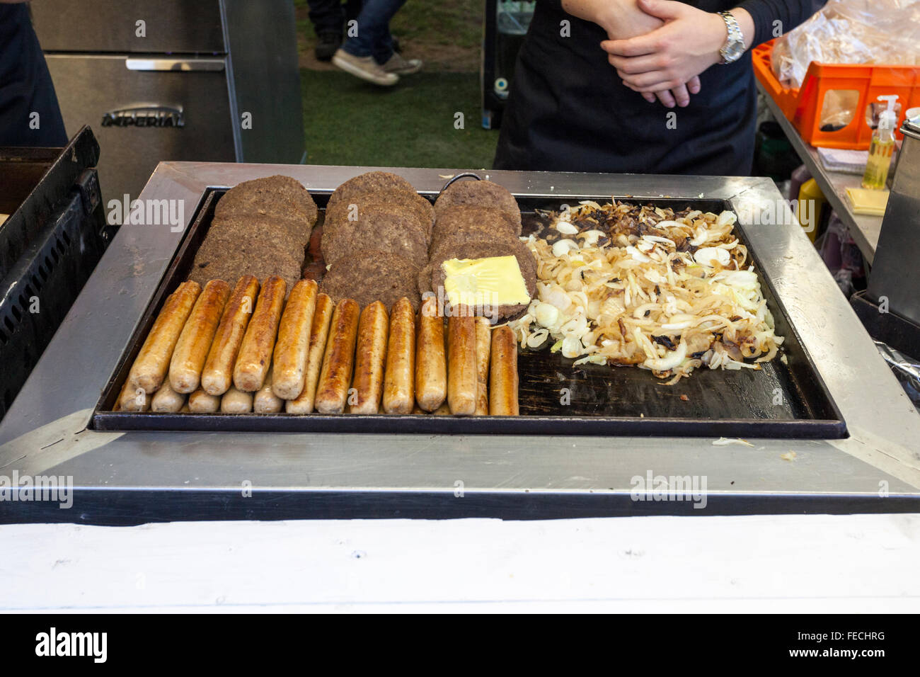 Outside catering. Hot dog sausages, burgers and onions cooking on a griddle at a fast food take away stall at Goose Fair, Nottingham, England, UK Stock Photo
