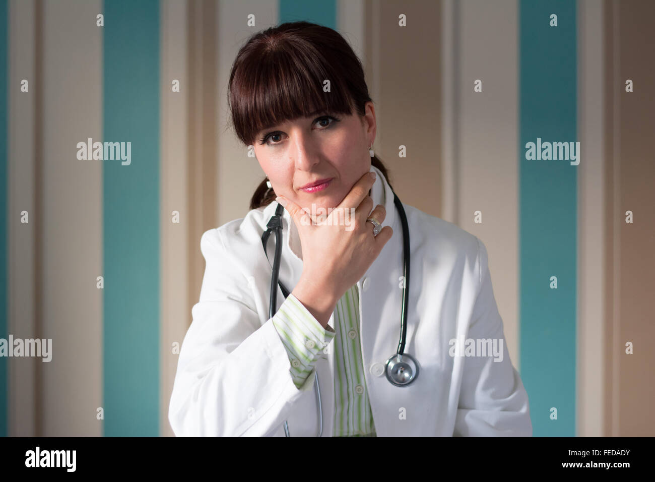 Female brunette doctor with bangs posing for the camera wearing scrubs and stethoscope Stock Photo