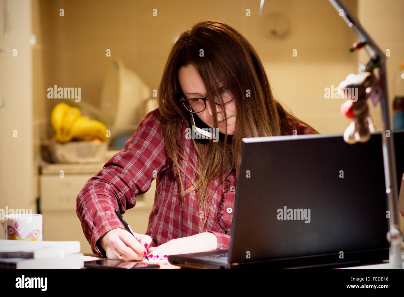 Young housewife paying bills online late in the evening after finishing all her house work, sitting at the desk with computer, b Stock Photo