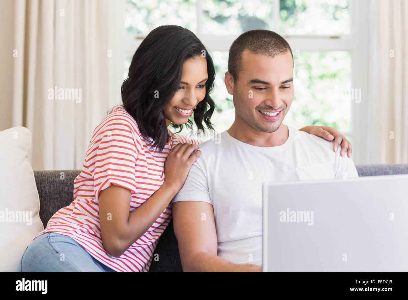 Smiling couple using laptop sitting on the couch Stock Photo - Alamy