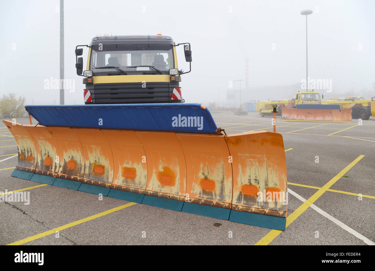 Snow removal vehicles and snowploughs with big dozer blades in autumn fog on standby for their duty at the airport runway Stock Photo