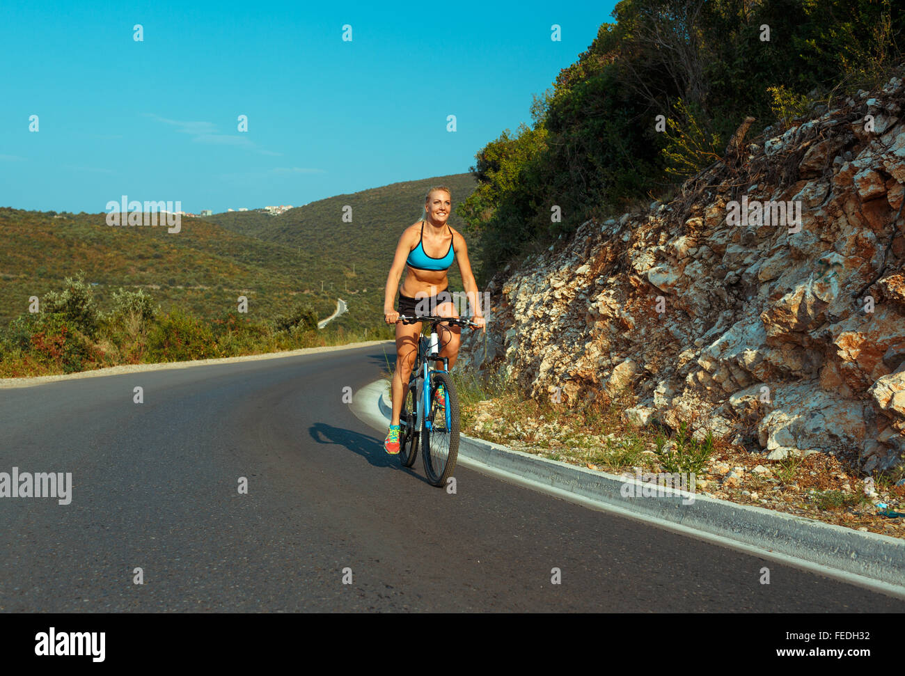 Happy woman cyclist riding a bike on a mountain road Stock Photo