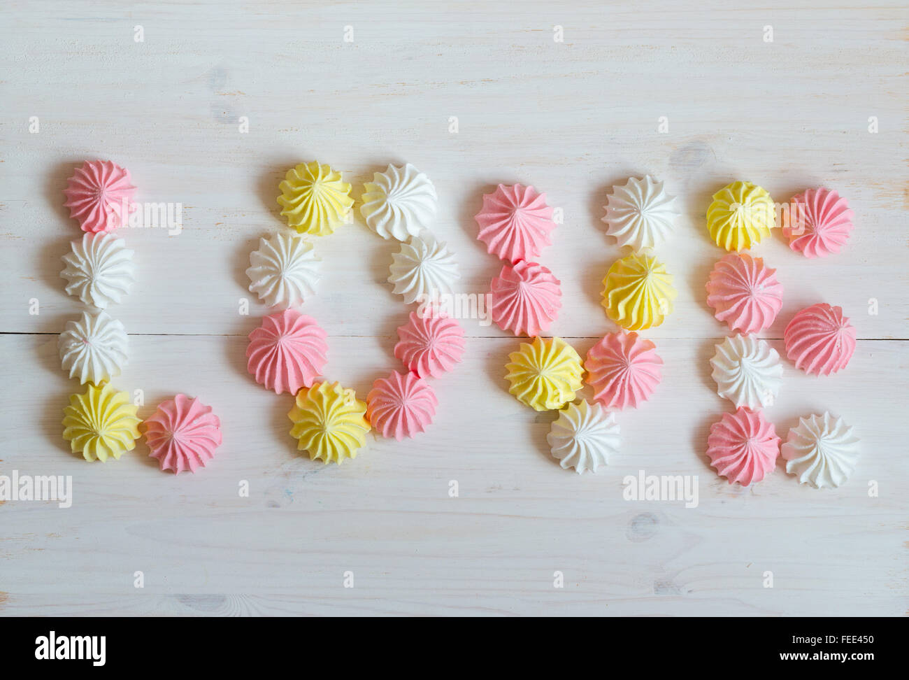 Inscription love meringue made of pastel colors on a white wooden background. Image of Valentines day Stock Photo