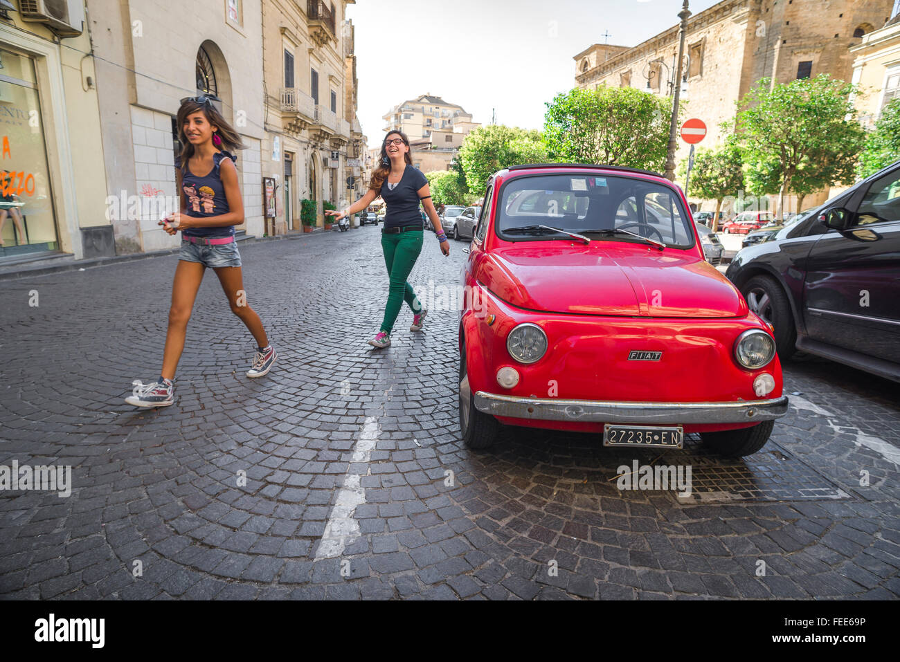 Fiat 500 Italy, view of two teenage women walking past a classic Fiat 500 Cinquecento parked in the Via Roma, Enna, Sicily. Stock Photo