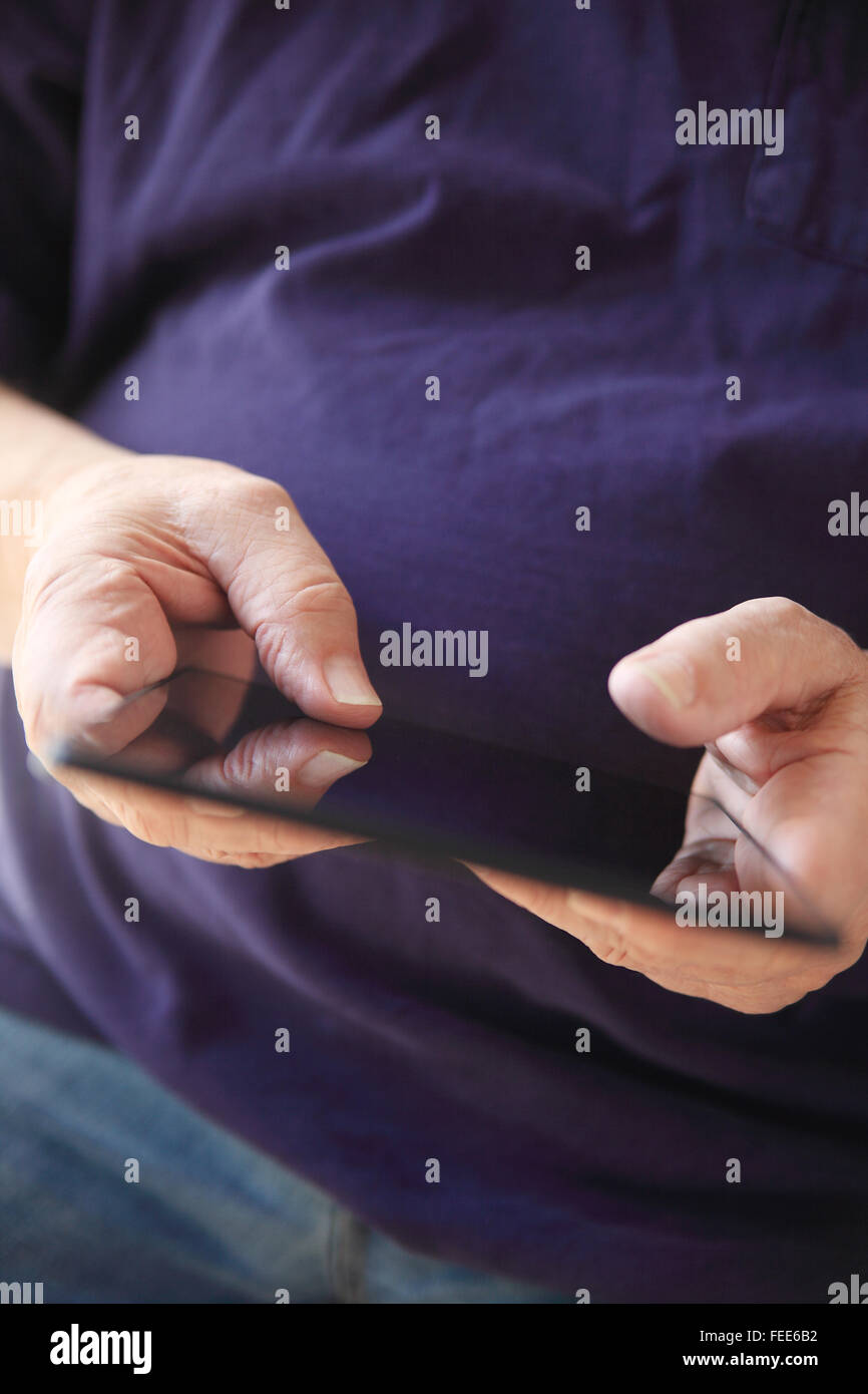 A man in a t-shirt uses his thumbs on a tablet. Stock Photo