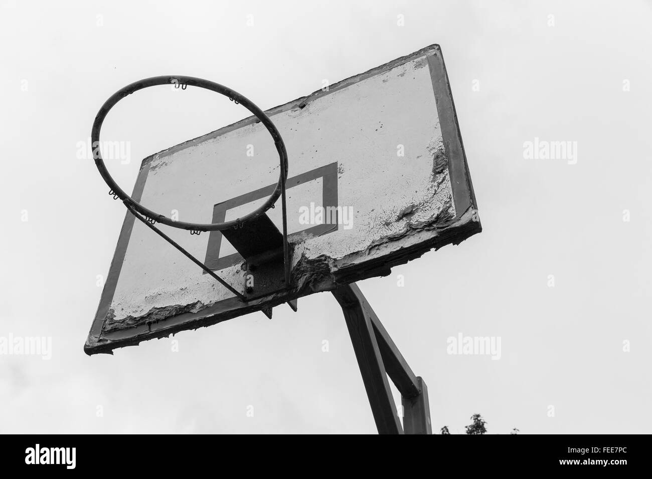 A black and white photo of an old basketball ring with a white wooden plate  where paint is peeling off and fixed to a steel pole Stock Photo - Alamy