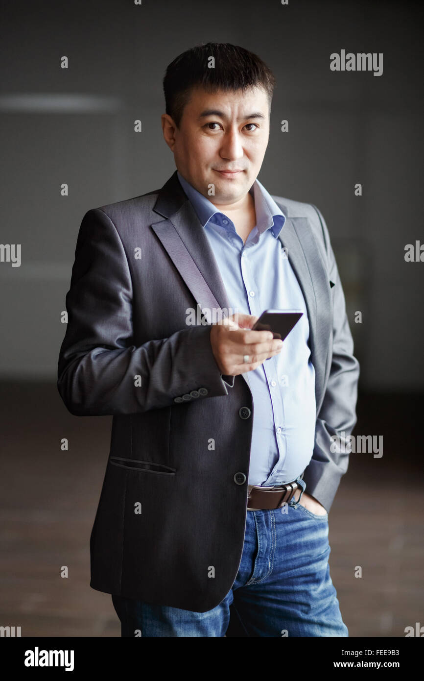 Serious brutal asian business man with phone in his hands, courageous suit portrait. Gray blue tones. Ready to go. Stock Photo