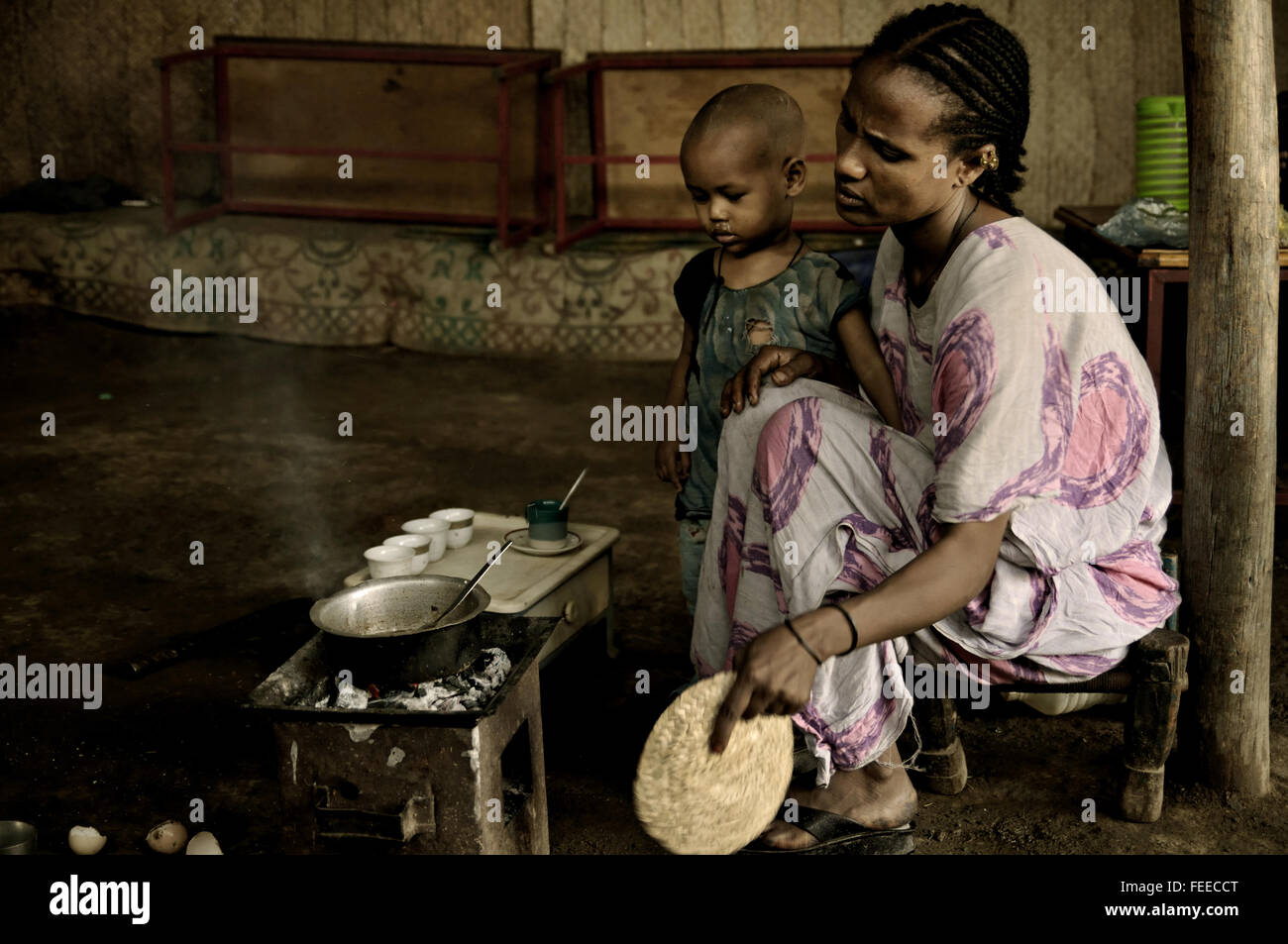 Ethiopian woman with her kid preparing freshly brewed coffee inside her house in Berhale, Afar Region, Ethiopia Stock Photo