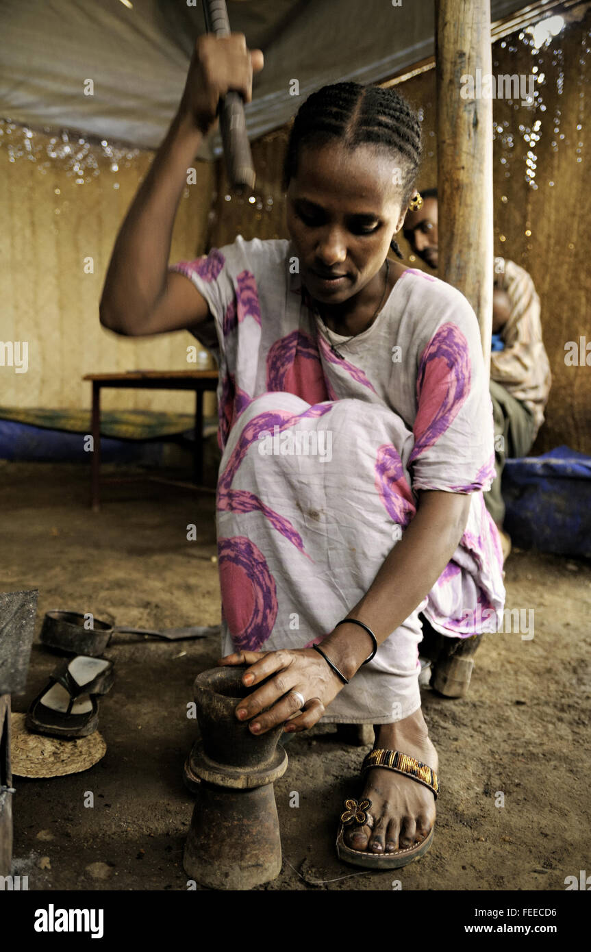 Woman grinding coffee beans inside a wooden mortar with a pestle in