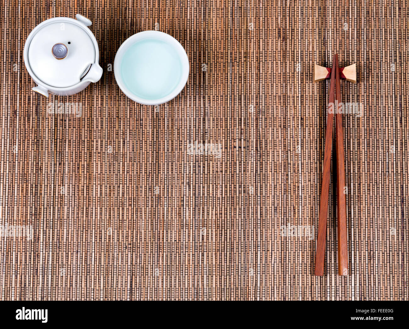 Overhead view of chopsticks, cup and tea server on bamboo mat. Stock Photo