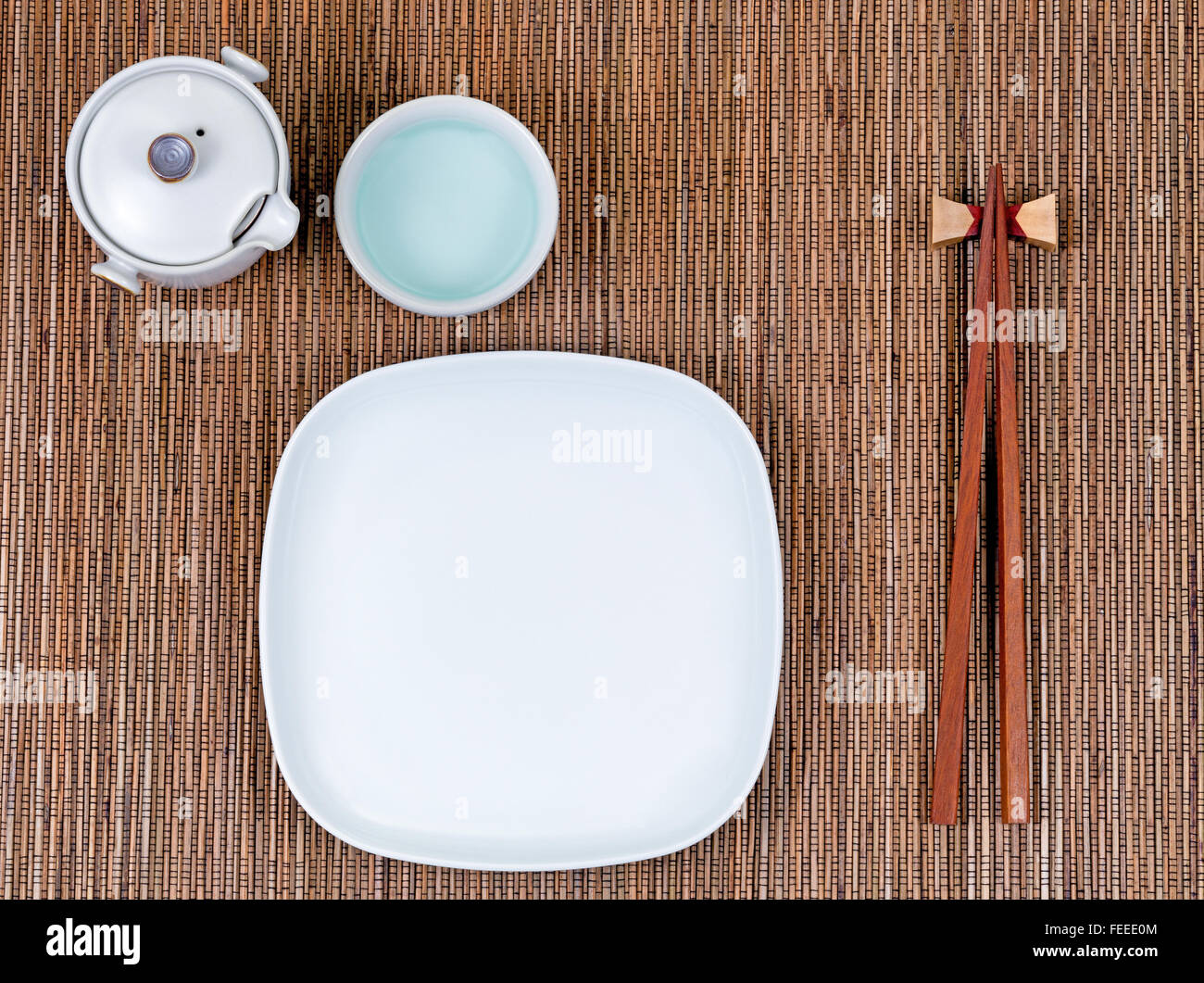 Overhead view of chopsticks, plate, cup and tea server on bamboo mat. Stock Photo