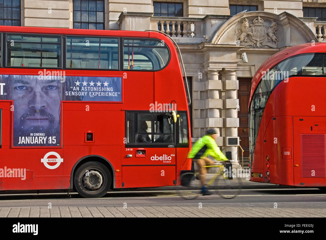 Cyclist wearing high visibility jacket passing red double decker buses on Whitehall in London. London buses are operated by Transport for London. Stock Photo