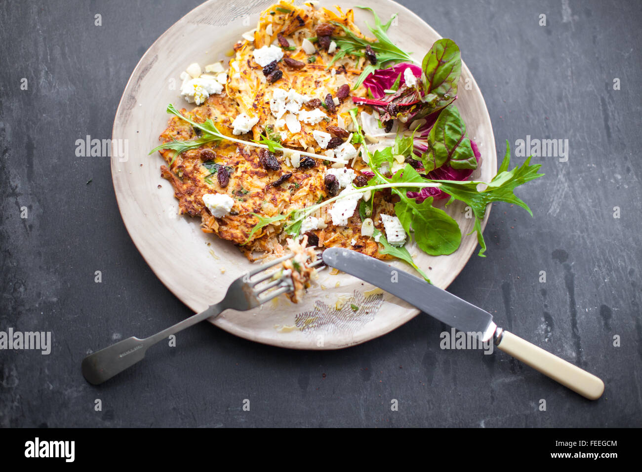 carrot, parsnip, chili and coriander rosti with organic salad, goats cheese, sultanas and flaked almonds. Stock Photo