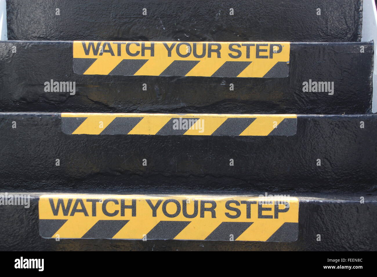 Yellow and black warning sign on stairs stating 'Watch your Step' signifying a potential trip hazard and steep stairs Stock Photo