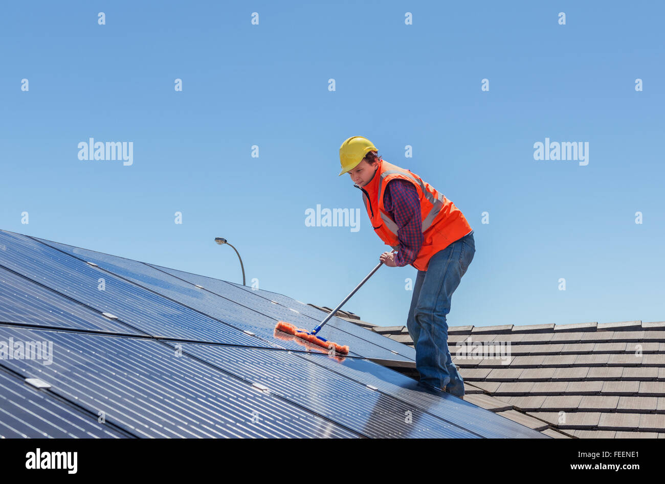 young worker cleaning solar panels on house roof Stock Photo