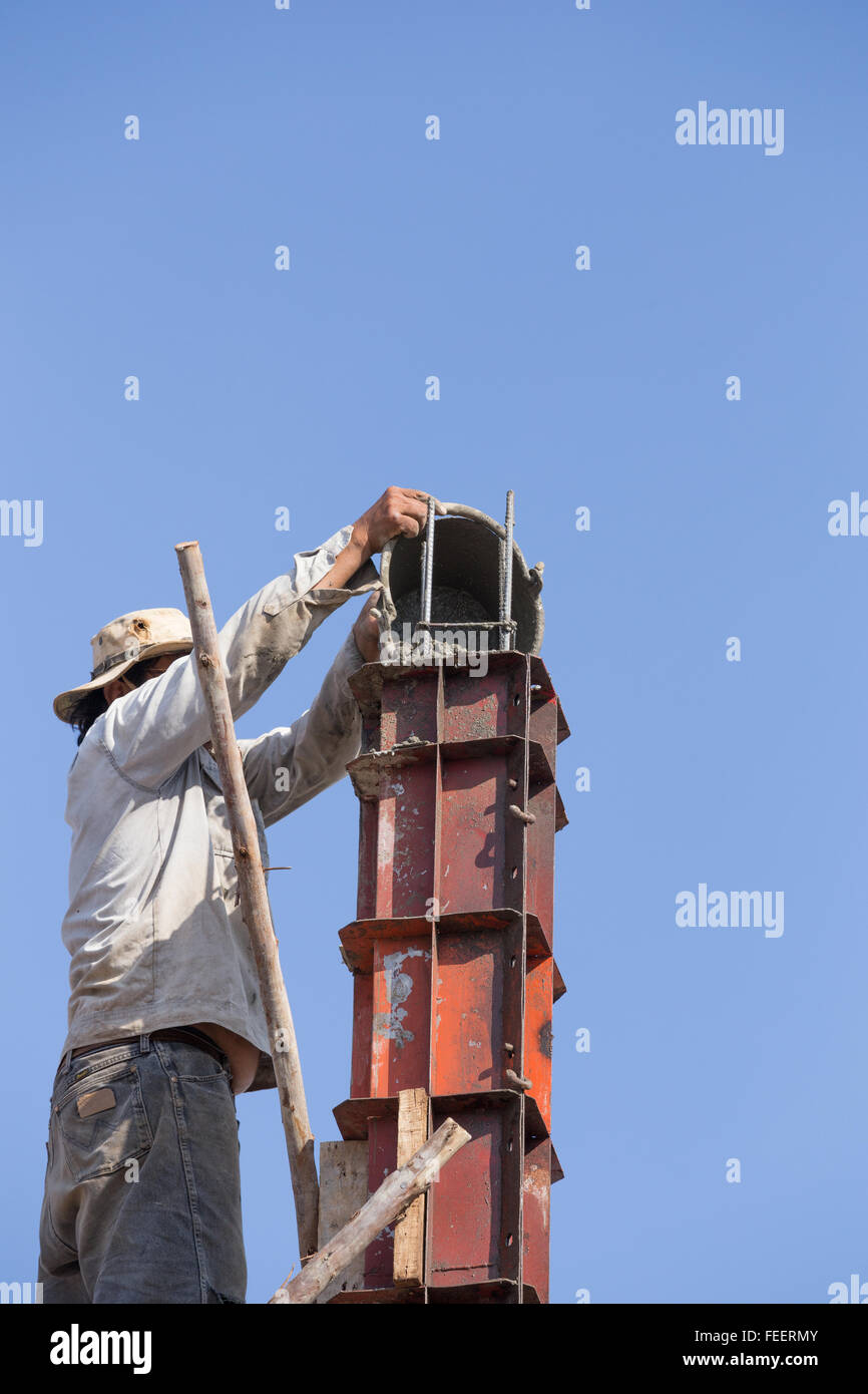 worker pouring cement to concrete pillar mold for house construction at