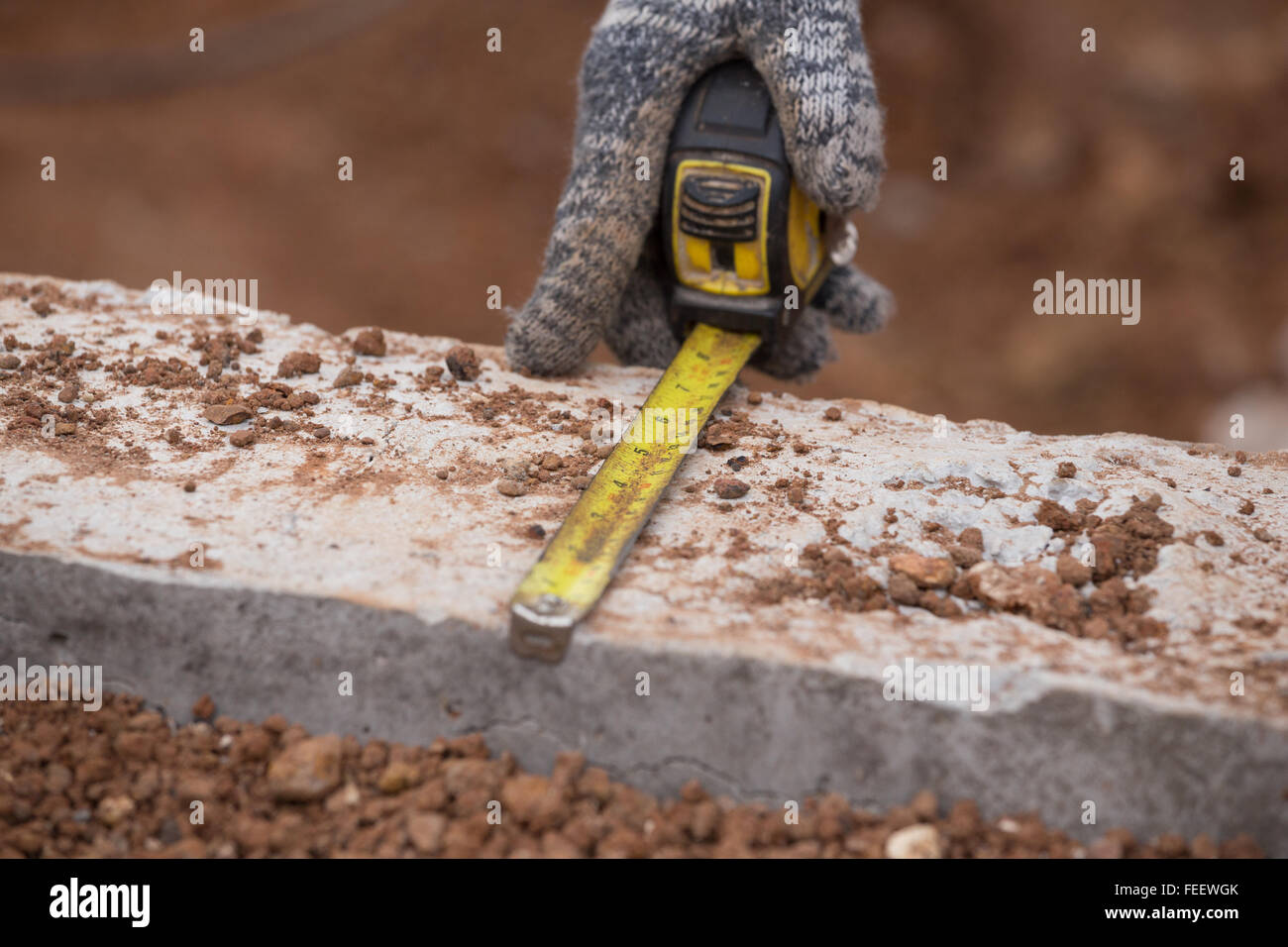 worker measuring concrete at construction site with tape measure Stock