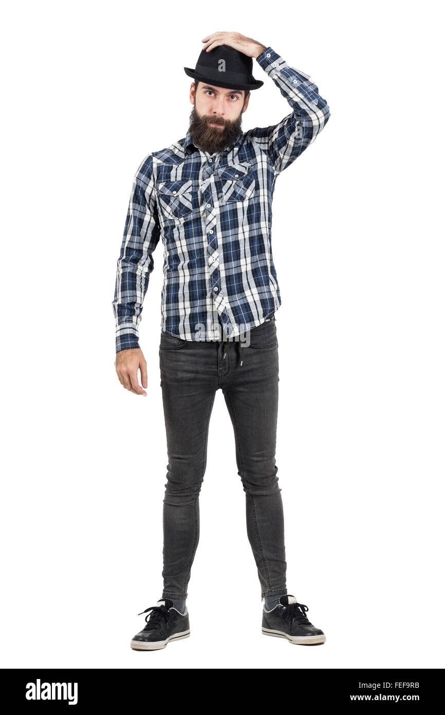 Bearded hipster putting on black fedora hat looking at camera. Full body length portrait isolated over white studio background. Stock Photo