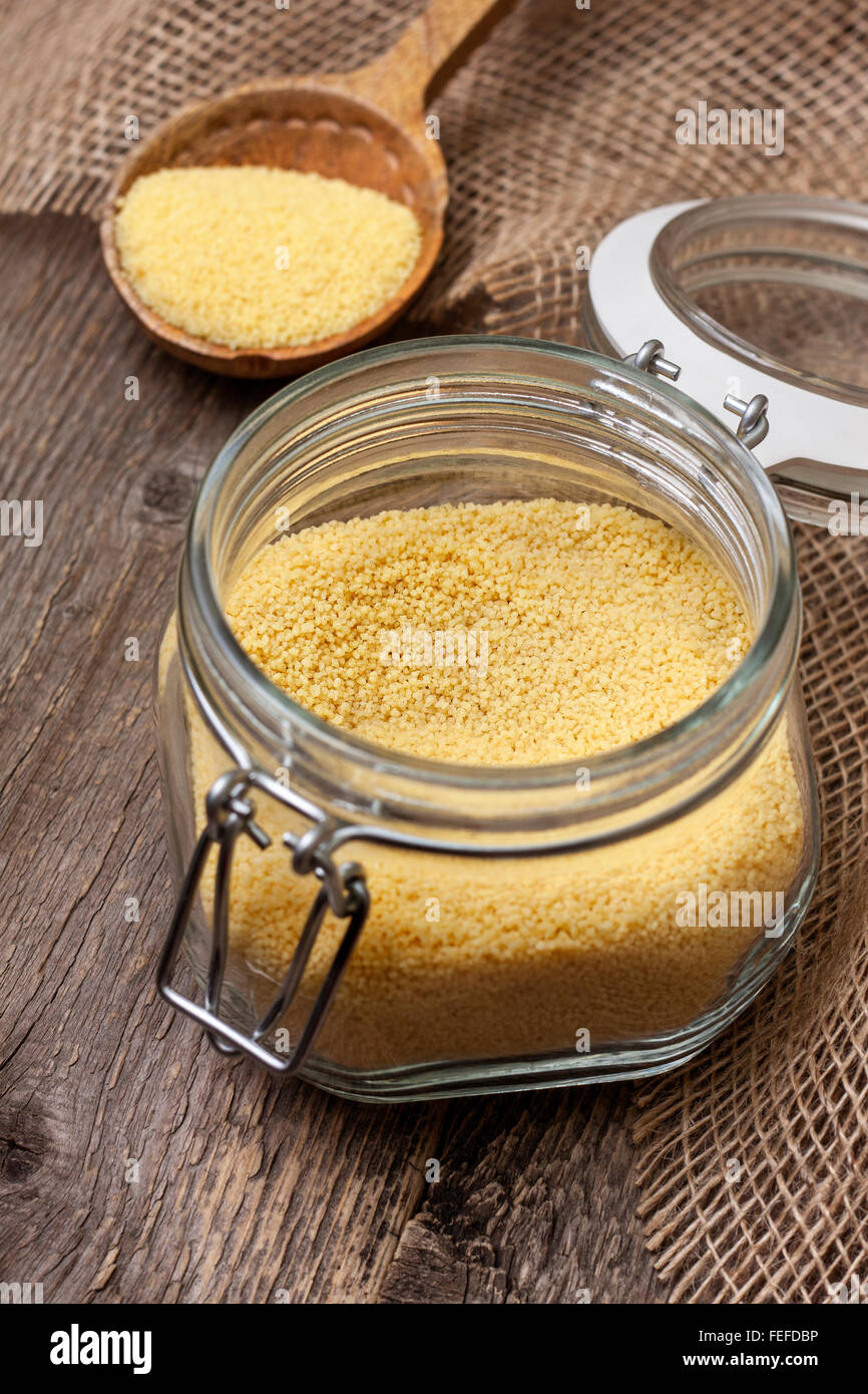 couscous in a glass jar on a wooden background, wooden spoon with couscous Stock Photo