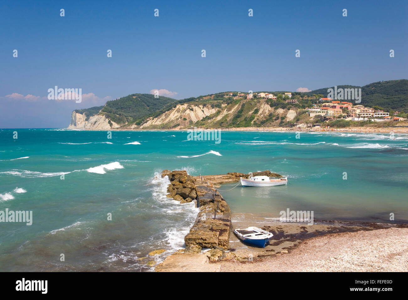Agios Stefanos (west), Corfu, Ionian Islands, Greece. View across rough turquoise sea, waves crashing against breakwater. Stock Photo
